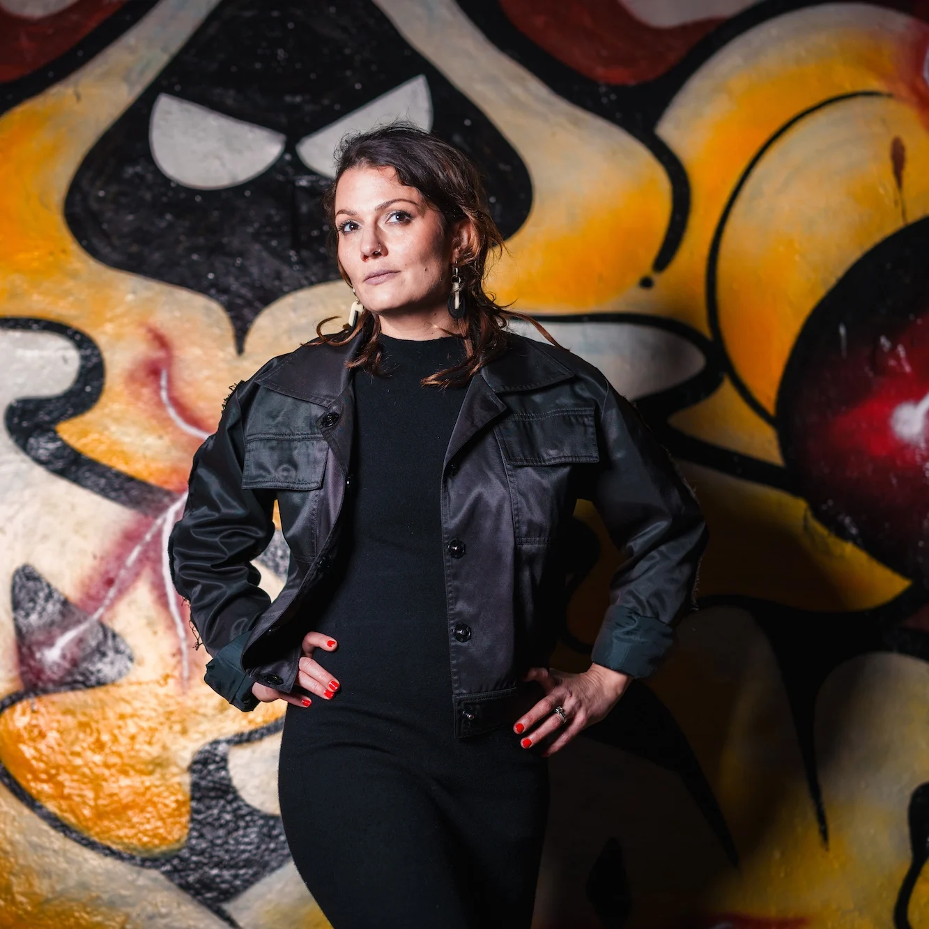 Rosanna Grüter ist schwarz angezogen und posiert vor einer Wand mir einem orange, gelblichen Graffity.